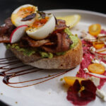 Best post workout breakfast in Sydney — open-faced sourdough with smashed avocado, crispy bacon and soft-boiled egg, served with beetroot sauce, cherry tomatoes, radish and feta at Cafe C&M