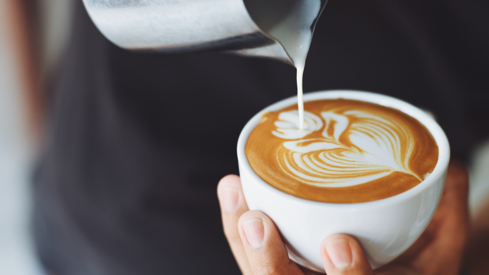 Close-up of hands pouring steamed milk to create latte art, highlighting coffee myths and facts at Cafe C&M Sydney.
