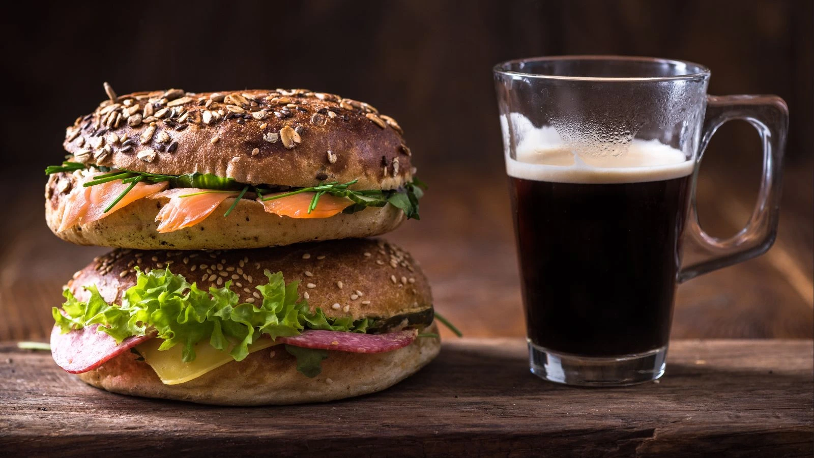 Two gourmet bagels stacked beside a glass of black coffee at Cafe C&M — best bagels and coffee in Sydney