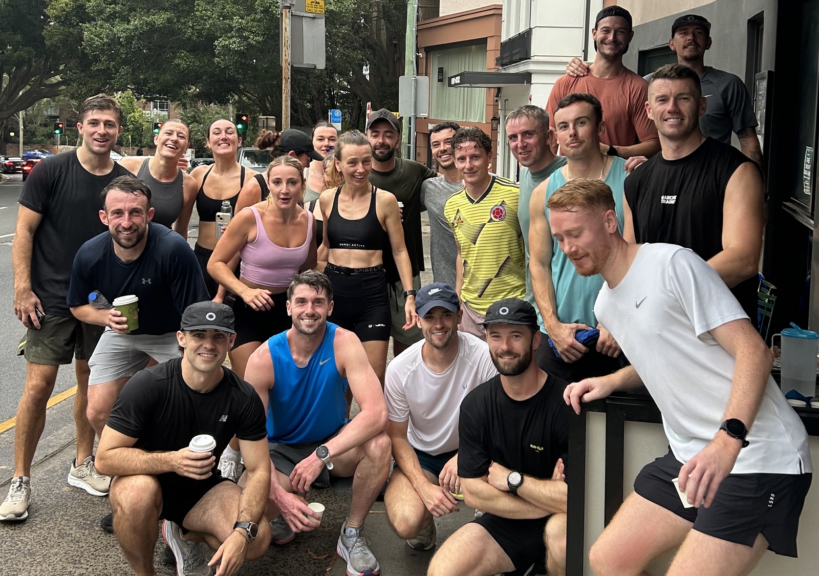 Group of runners gathered outside Cafe C&M Bondi after a session with the Forge Focus Sunday running club Bondi, holding takeaway coffees and smiling post-run.