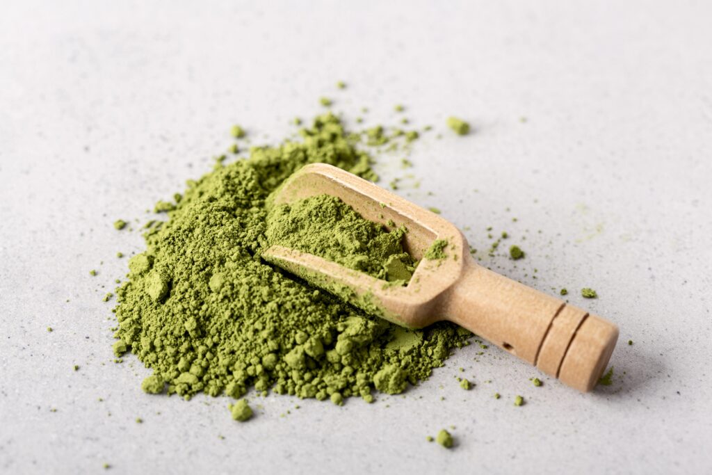 Close-up of vibrant green matcha powder with a wooden scoop on a light stone surface, showing premium matcha used in Cafe C&M iced matcha drinks.